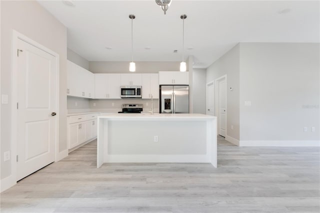kitchen with stainless steel appliances, light countertops, white cabinets, hanging light fixtures, and light wood finished floors