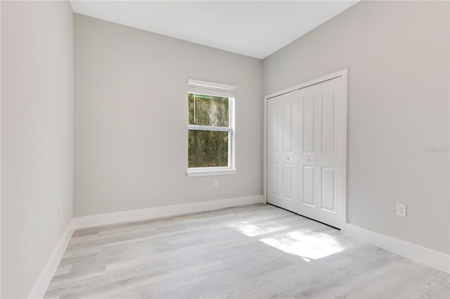 unfurnished bedroom with light wood-type flooring, baseboards, and a closet