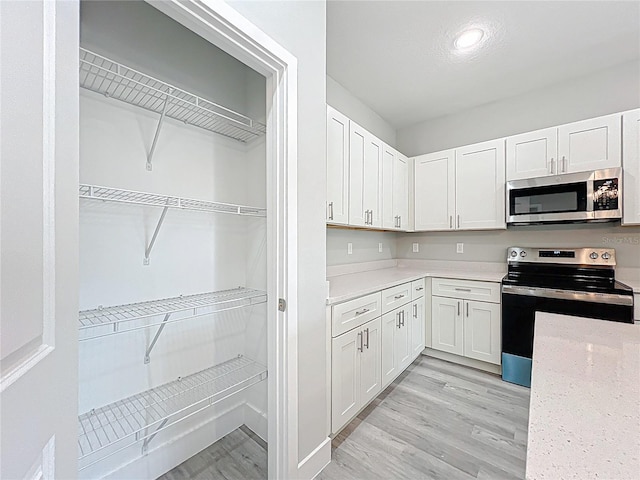 2531 SW 167th Loop, Ocala, FL 34473 - kitchen with appliances with stainless steel finishes, white cabinets, light wood-style floors, light stone countertops, and recessed lighting