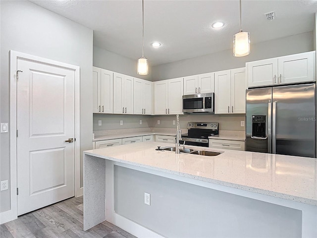 2531 SW 167th Loop, Ocala, FL 34473 - kitchen featuring stainless steel appliances, white cabinets, light wood-style flooring, decorative light fixtures, and light stone countertops