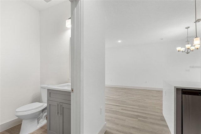 bathroom featuring vanity, a chandelier, toilet, wood finished floors, and baseboards