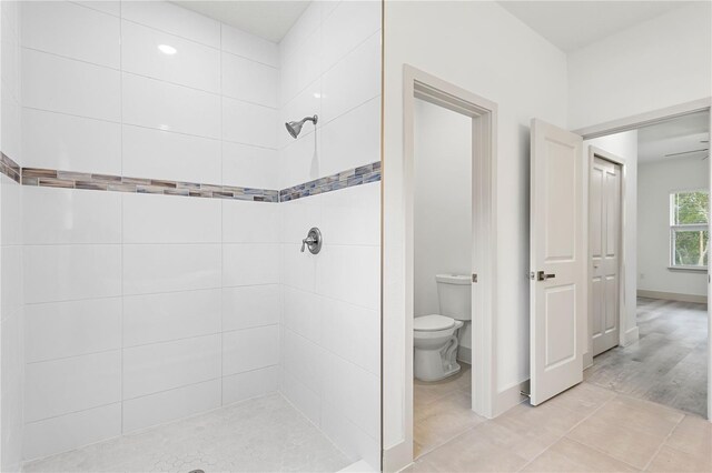 full bath with a tile shower, toilet, and baseboards