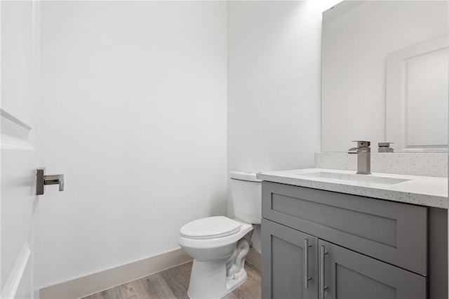 half bathroom featuring toilet, wood finished floors, vanity, and baseboards