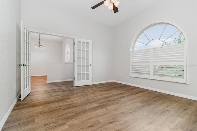 unfurnished room featuring french doors, a chandelier, a ceiling fan, wood finished floors, and baseboards