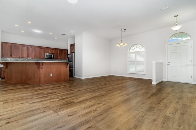 unfurnished living room with a chandelier, wood finished floors, recessed lighting, and baseboards