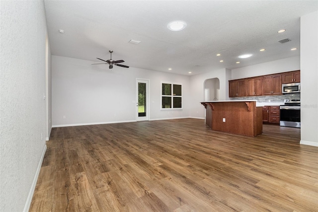 kitchen featuring stainless steel appliances, open floor plan, a breakfast bar area, arched walkways, and dark wood-style floors