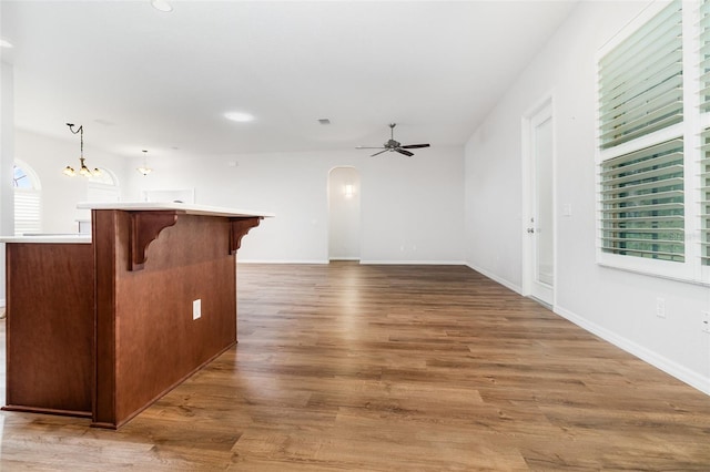 unfurnished living room with arched walkways, ceiling fan, a chandelier, light wood-type flooring, and baseboards