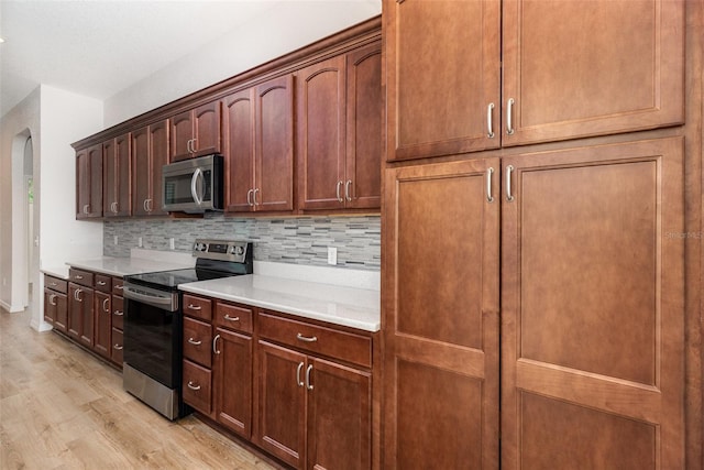kitchen featuring appliances with stainless steel finishes, light wood-type flooring, backsplash, light countertops, and arched walkways