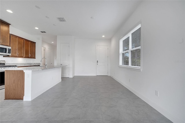 kitchen with appliances with stainless steel finishes, recessed lighting, an island with sink, a sink, and baseboards