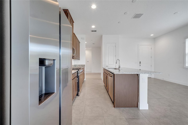 kitchen featuring appliances with stainless steel finishes, a sink, light tile patterned floors, recessed lighting, and a center island with sink