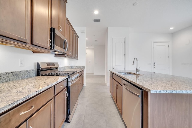 kitchen featuring stainless steel appliances, a sink, a center island with sink, light stone countertops, and recessed lighting