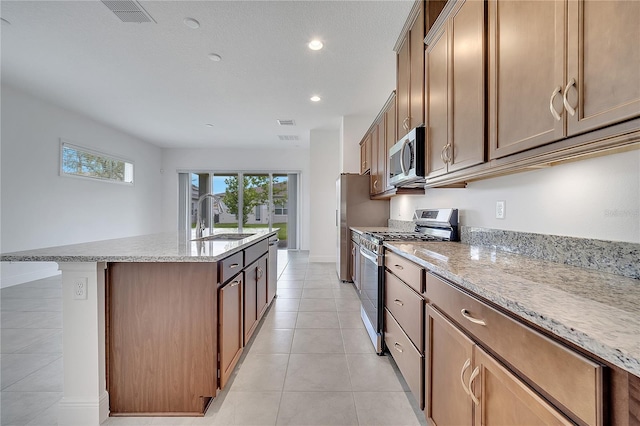 kitchen with appliances with stainless steel finishes, a sink, a center island with sink, light stone counters, and recessed lighting