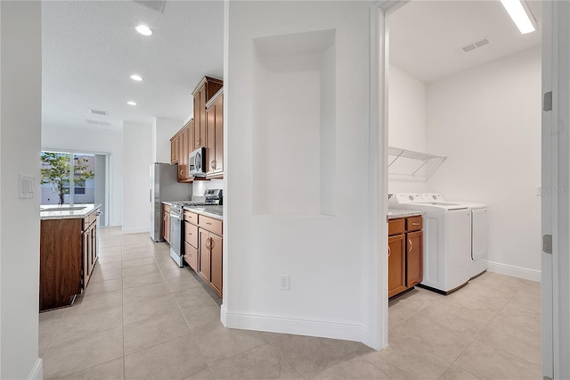 kitchen featuring stainless steel appliances, a sink, washing machine and dryer, light countertops, and brown cabinetry