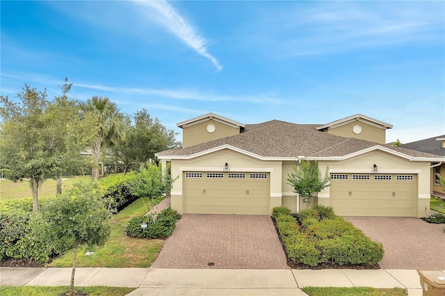 traditional home featuring stucco siding, decorative driveway, an attached garage, and a shingled roof
