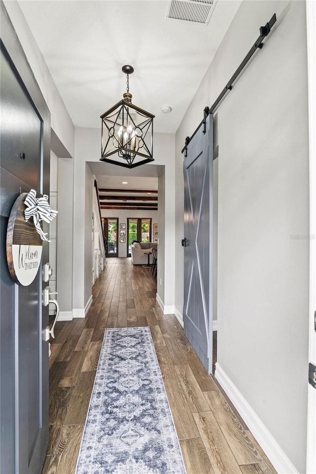 foyer entrance featuring a barn door, baseboards, dark wood-type flooring, and a chandelier