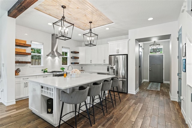 kitchen featuring open shelves, stainless steel appliances, wall chimney exhaust hood, a chandelier, and plenty of natural light