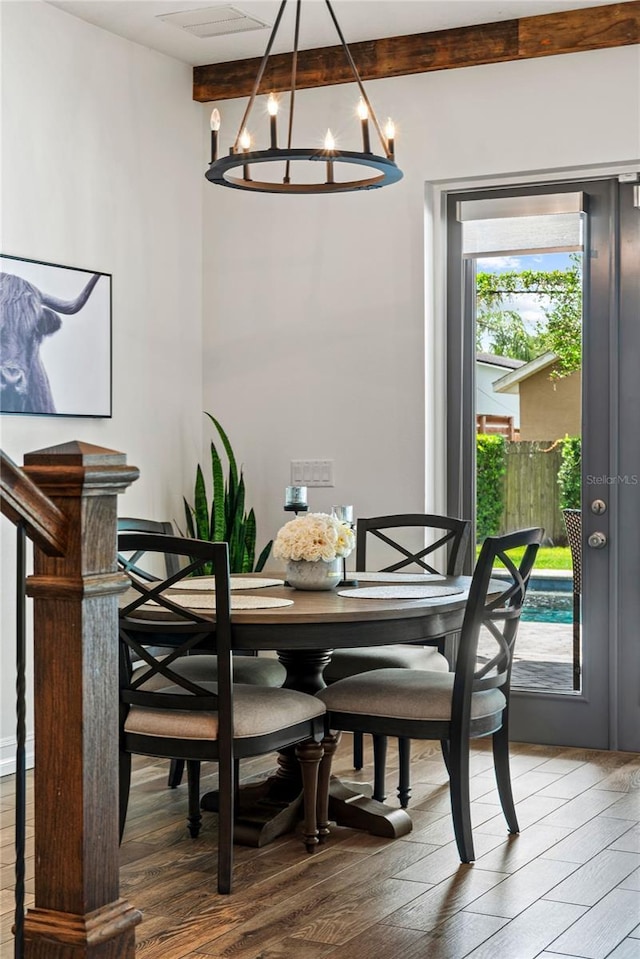 dining space with wood finished floors, a chandelier, and beamed ceiling