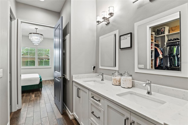 full bath with wood finished floors, a chandelier, double vanity, and baseboards