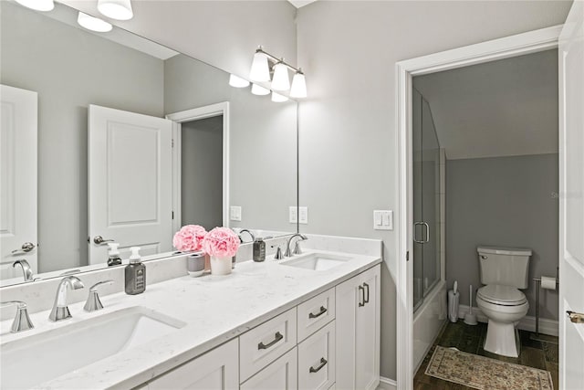 full bath with toilet, double vanity, combined bath / shower with glass door, wood finished floors, and baseboards