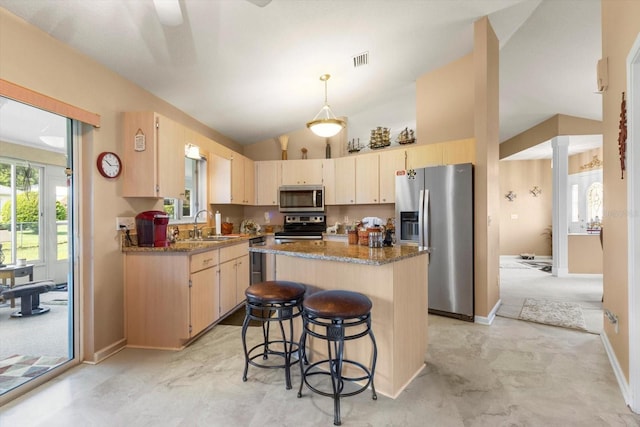 kitchen featuring stainless steel appliances, light brown cabinets, a kitchen island, a sink, and a breakfast bar