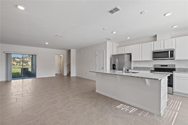 17081 Water Spring Blvd, Winter Garden, FL 34787 - kitchen featuring appliances with stainless steel finishes, a center island with sink, light stone counters, a textured ceiling, and open floor plan