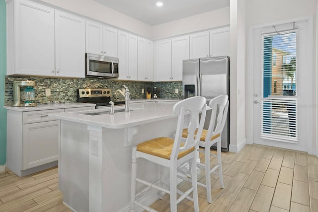 8045 Lost Shaker Ln, Kissimmee, FL 34747 - kitchen featuring stainless steel appliances, light countertops, backsplash, white cabinetry, and a kitchen breakfast bar
