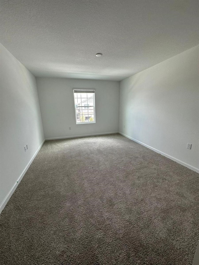empty room with carpet, baseboards, and a textured ceiling