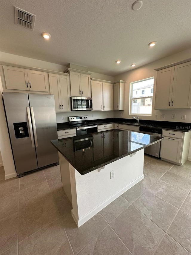 kitchen featuring appliances with stainless steel finishes, a sink, a kitchen island, recessed lighting, and a textured ceiling