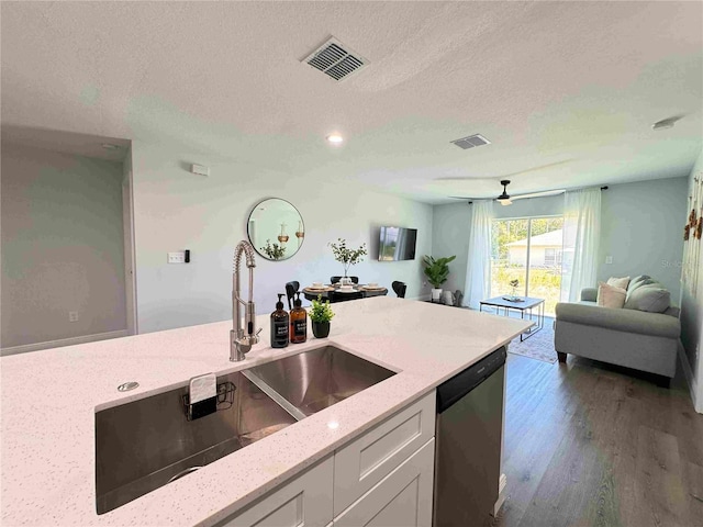 kitchen with dishwasher, a sink, a textured ceiling, dark wood-style floors, and light stone counters