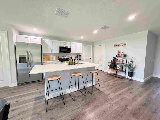 kitchen with stainless steel appliances, white cabinets, a kitchen island with sink, a breakfast bar, and light wood-style flooring