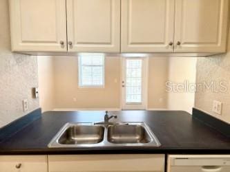 kitchen with dishwasher, a sink, dark countertops, and white cabinets