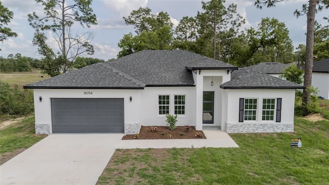 view of front of home with roof with shingles, an attached garage, concrete driveway, stucco siding, and a front lawn