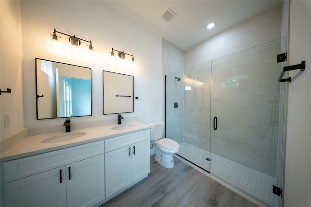 full bath featuring wood finished floors, a stall shower, double vanity, and toilet