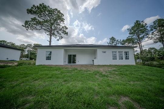 rear view of house featuring a yard and stucco siding