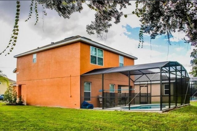 rear view of house with stucco siding, a yard, an outdoor pool, and glass enclosure