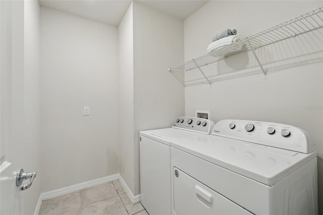 clothes washing area featuring washing machine and clothes dryer, baseboards, and light tile patterned flooring