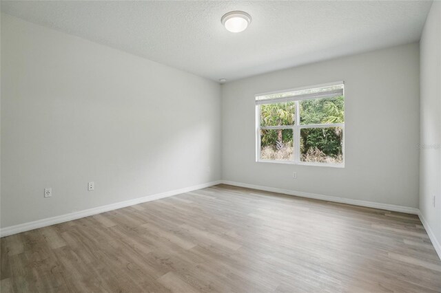 unfurnished room featuring light wood-style flooring, baseboards, and a textured ceiling