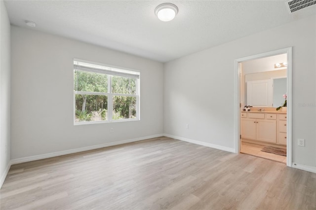 unfurnished bedroom featuring light wood-type flooring, baseboards, and ensuite bath