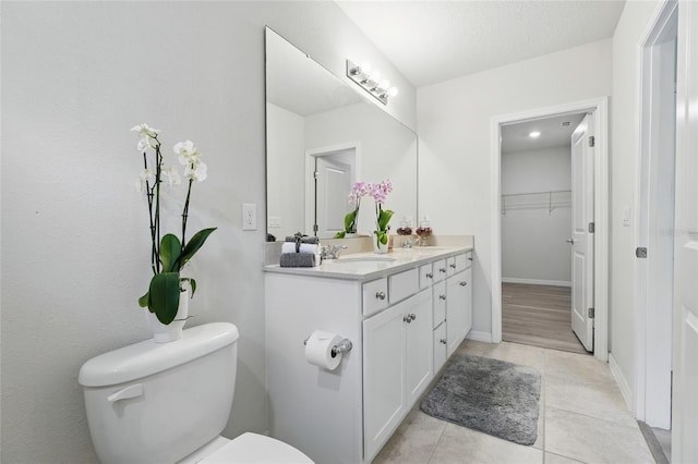 bathroom with toilet, tile patterned floors, double vanity, baseboards, and a spacious closet
