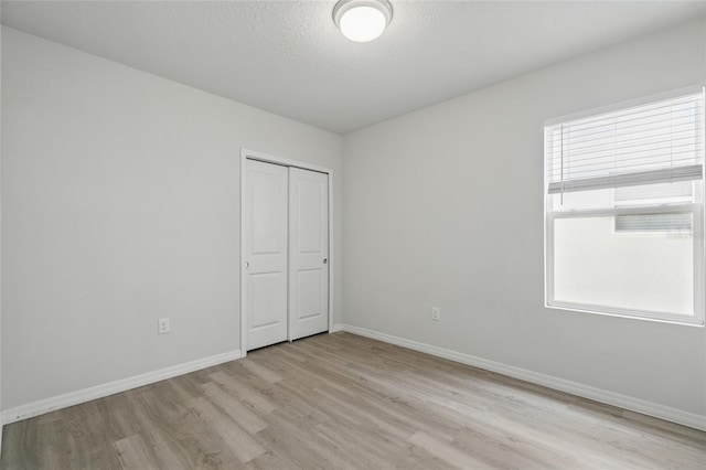unfurnished bedroom with light wood-style flooring, baseboards, a closet, and a textured ceiling
