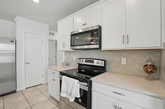 kitchen featuring stainless steel appliances, light tile patterned floors, white cabinetry, and backsplash