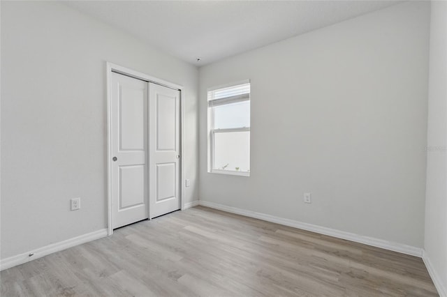 unfurnished bedroom with light wood-type flooring, baseboards, and a closet