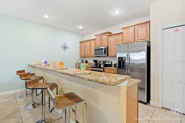 8941 Bismarck Palm Rd, Kissimmee, FL 34747 - kitchen with stainless steel appliances, a kitchen breakfast bar, light tile patterned floors, light stone countertops, and baseboards