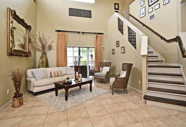 tiled living room with a towering ceiling, baseboards, and stairs