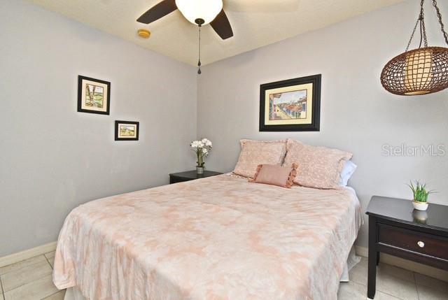 bedroom featuring baseboards, light tile patterned floors, and a ceiling fan