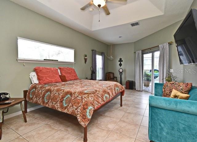 bedroom featuring access to outside, light tile patterned floors, a tray ceiling, and a ceiling fan