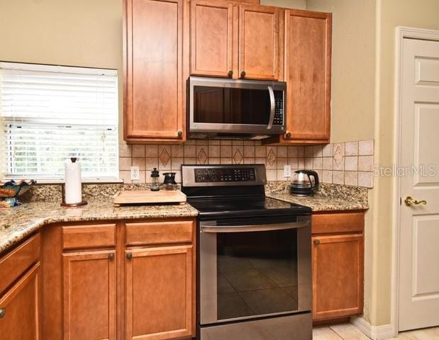 kitchen featuring stainless steel appliances, tasteful backsplash, light stone countertops, and brown cabinets