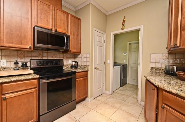 kitchen featuring stainless steel appliances, separate washer and dryer, crown molding, decorative backsplash, and light tile patterned floors