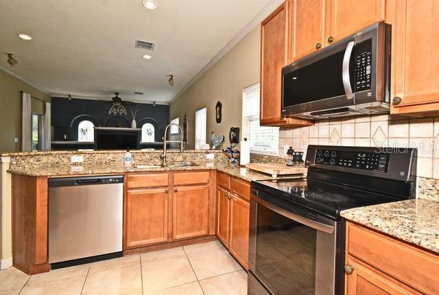 kitchen featuring appliances with stainless steel finishes, a sink, a peninsula, ornamental molding, and tasteful backsplash