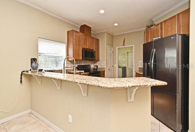 kitchen featuring black appliances, light tile patterned floors, a peninsula, brown cabinetry, and ornamental molding